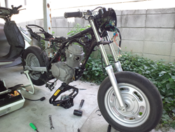そしてエンジン搭載のため、ベンアペは石川遼クンの地元として知られる、埼玉県松伏町にある通称・MBB（松伏ベース）へ。ちょうど１年ほど前、不幸なアクシデントhttp://www.m-bike.sakura.ne.jp/feature/roots/04.html に遭遇してからMBBで休眠状態にあったXLR80Rからエンジンを移植することに。G2連邦委託テクニカル・ディレクターであり、MBB管理人・ツボ８さんの協力によって、搭載作業はあっさり完了。エンジン側の配線端子をエイプ側のハーネスに合わせて繋ぎ、キックすること数回。79cc縦型ユニットは快音を伴い目を覚ましました。「Ape80」が誕生した瞬間です。